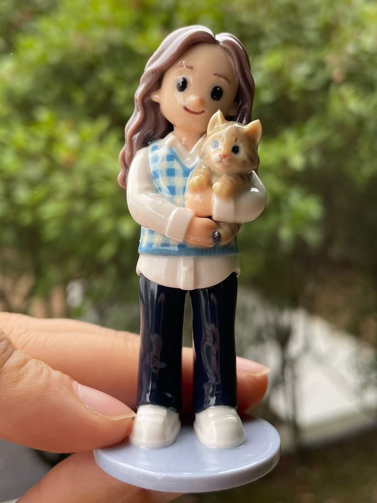 Figurine of a girl in a checked vest cradling her ginger cat
